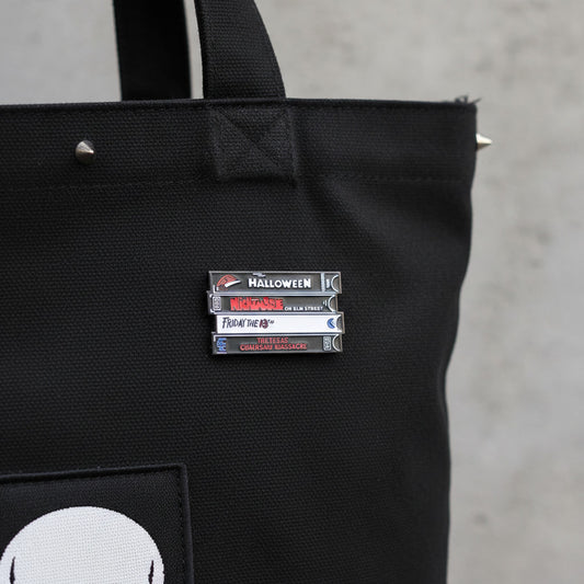 Black tote bag with a horror movie vhs tape enamel pin on a concrete surface