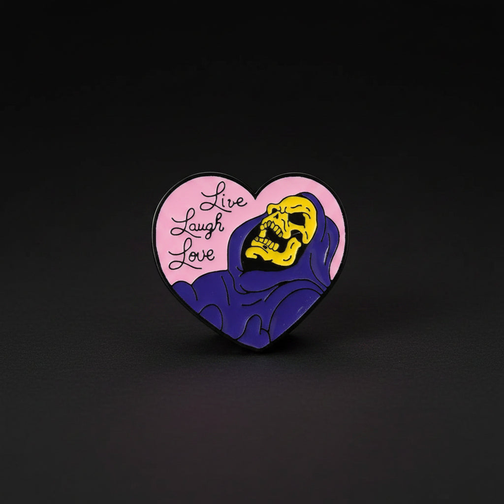 A black toned metal heart shaped pin with the phrase Live, Laugh, Love on a pink background and an image of Skeletor.